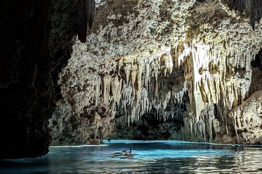 A cave with stalactites and stalagmites, a pool of water, and a person kayaking. 2