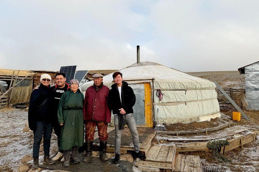 A group of people standing in front of a yurt with a solar panel and wooden structures in a snowy landscape. 1