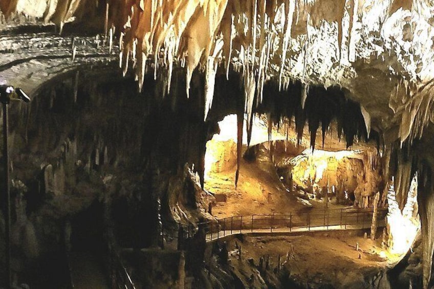 A cave with stalactites and stalagmites, a dirt path, and a small pool of water. 4