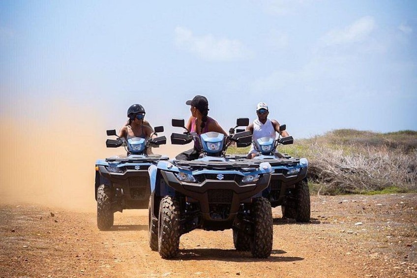 Drie personen rijden op quads over een zandpad, met een heldere lucht. 2