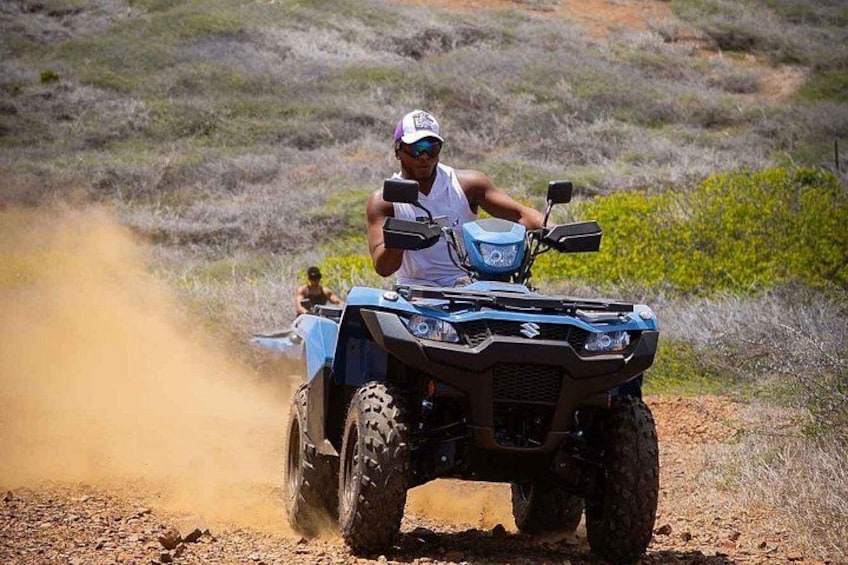 A person riding a blue ATV on a dirt path with dust being kicked up. 1