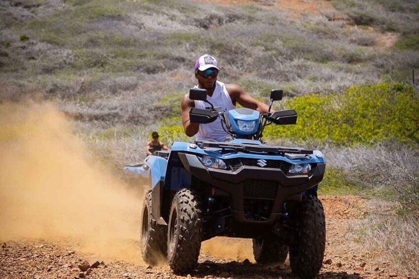 Une personne conduit un quad bleu sur un chemin de terre, et la poussière se soulève. 1