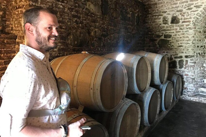 A person standing next to stacked wooden barrels in a cellar with stone walls. 2