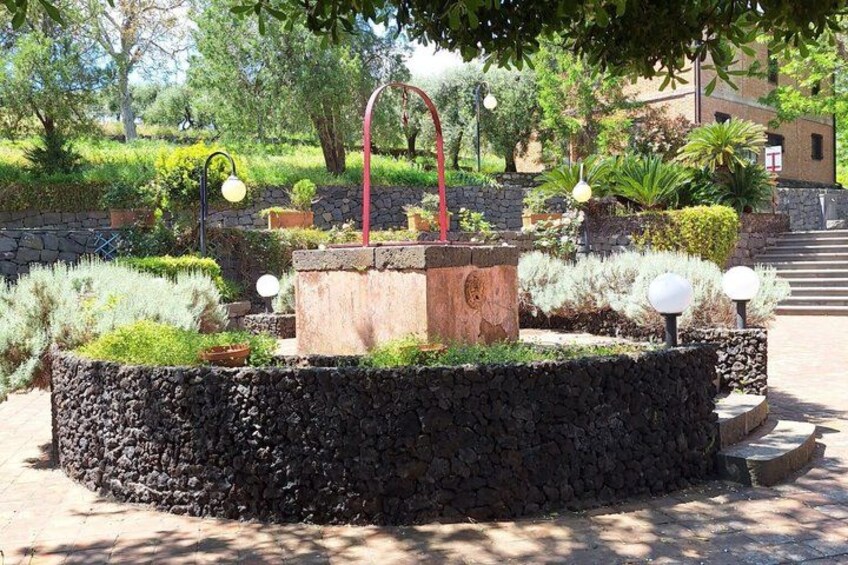 Un giardino con una fontana al centro, muri in pietra e diverse piante. 3