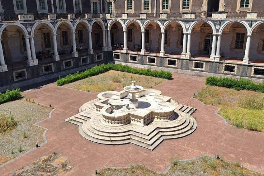 Un patio con una fuente central, rodeado de arcos y un jardín. 5