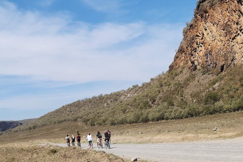 En gruppe cyklister på en asfalteret vej med et bjergrigt landskab i baggrunden. 4