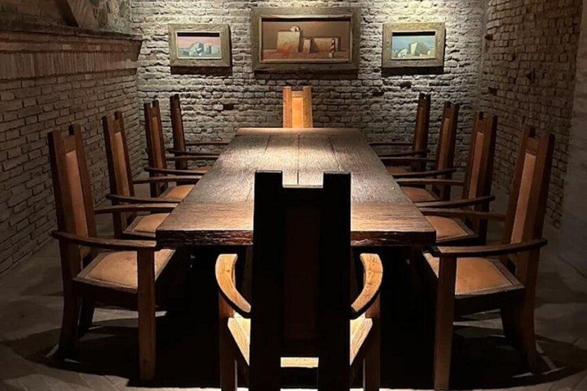 Una larga mesa de madera con sillas en una habitación con paredes de piedra y cuadros enmarcados. 3