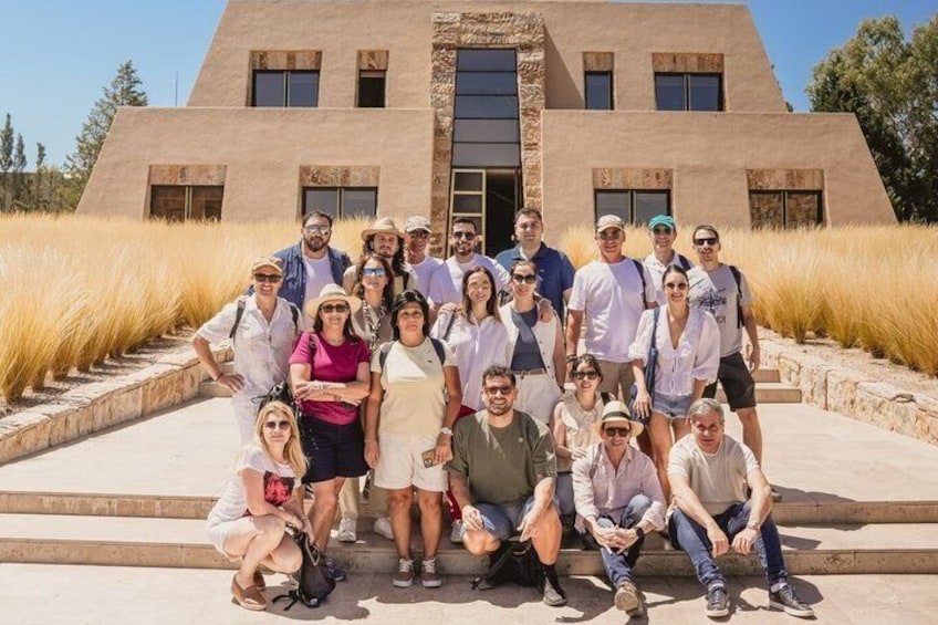 Un grupo de personas posando frente a un edificio moderno con un diseño arquitectónico distintivo, rodeado de pastos altos. 1