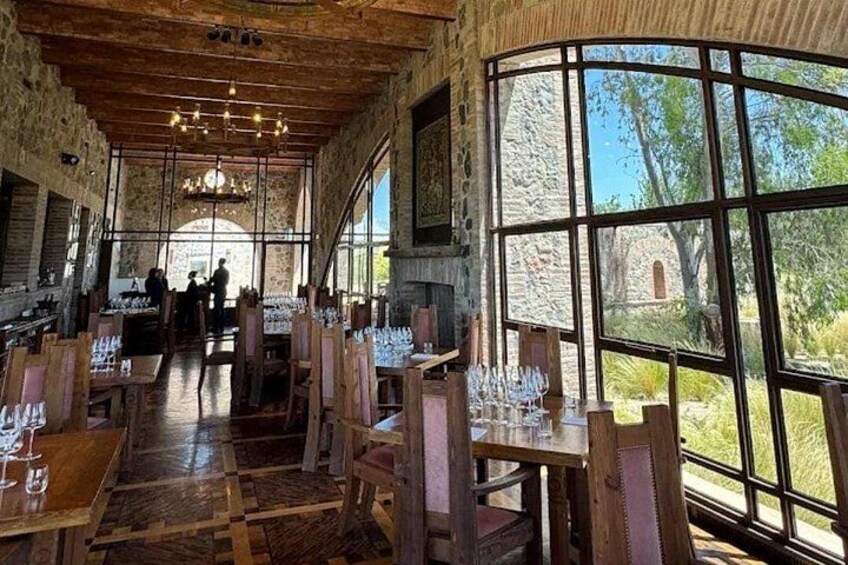 Un comedor interior con mesas y sillas de madera, ventanas amplias y una pared de piedra. 4