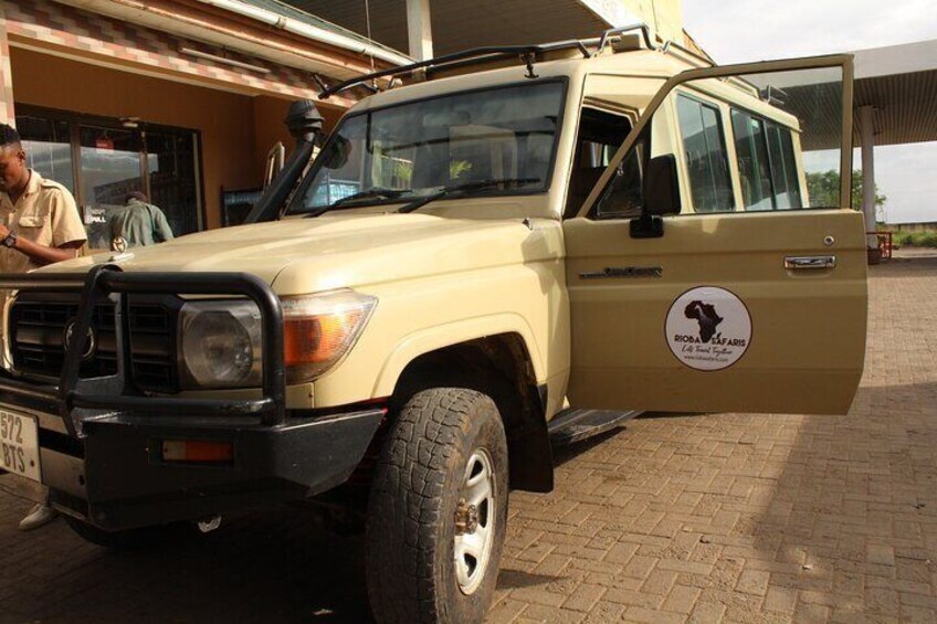 A beige safari vehicle parked in front of a building with a logo on the side. 2