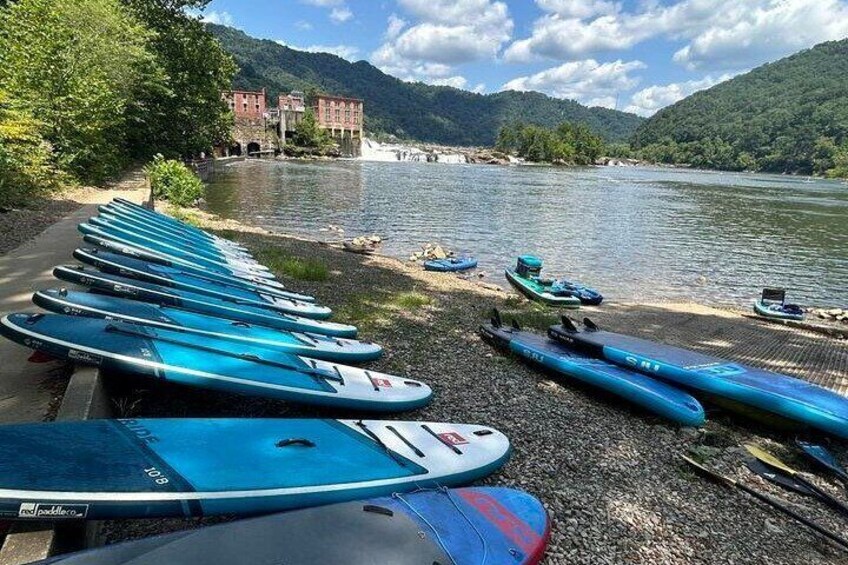 Una fila di tavole da paddleboard blu allineate su un vialetto sterrato lungo un fiume. 5