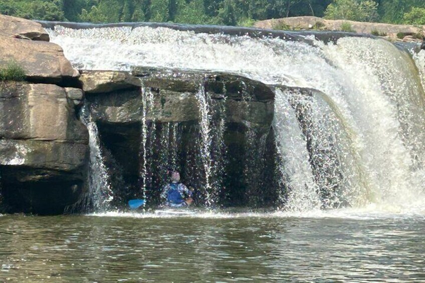 Una cascata che si getta su rocce in un corpo d'acqua, con una persona con un giubbotto blu in piedi nell'acqua. 1