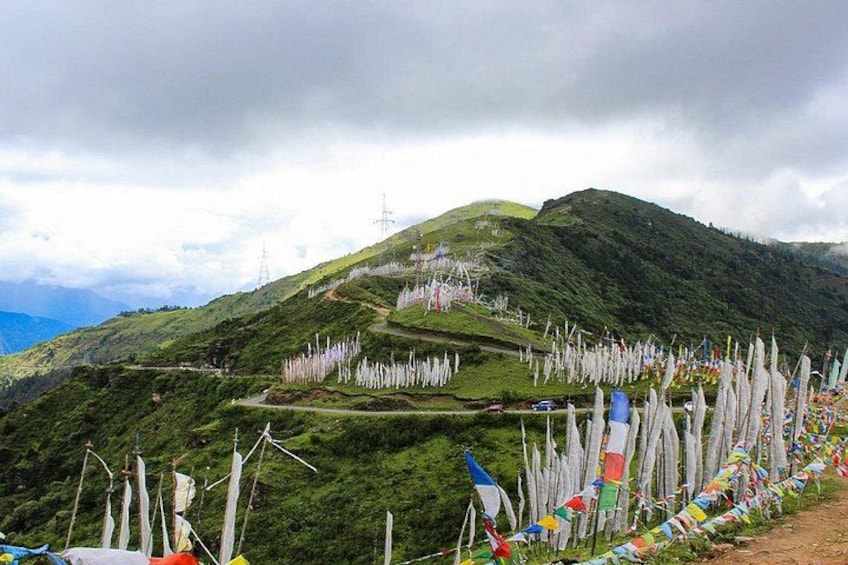 A mountainous landscape with a dirt path, prayer flags, and wind turbines. 1