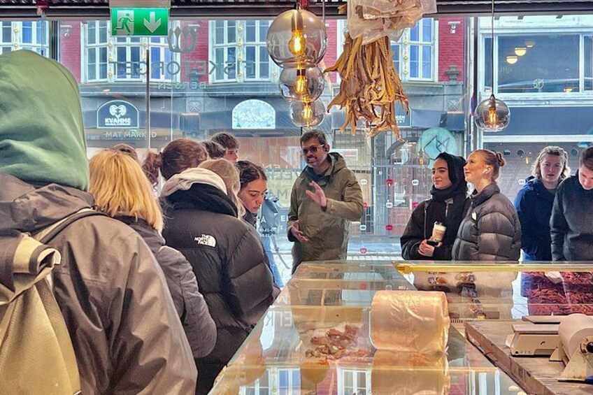 A group of people inside a shop with a glass counter displaying food items. 3