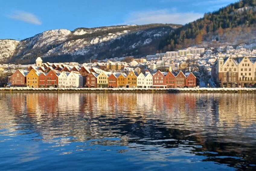 A row of colorful houses by a calm lake with snow-covered hills in the background. 1