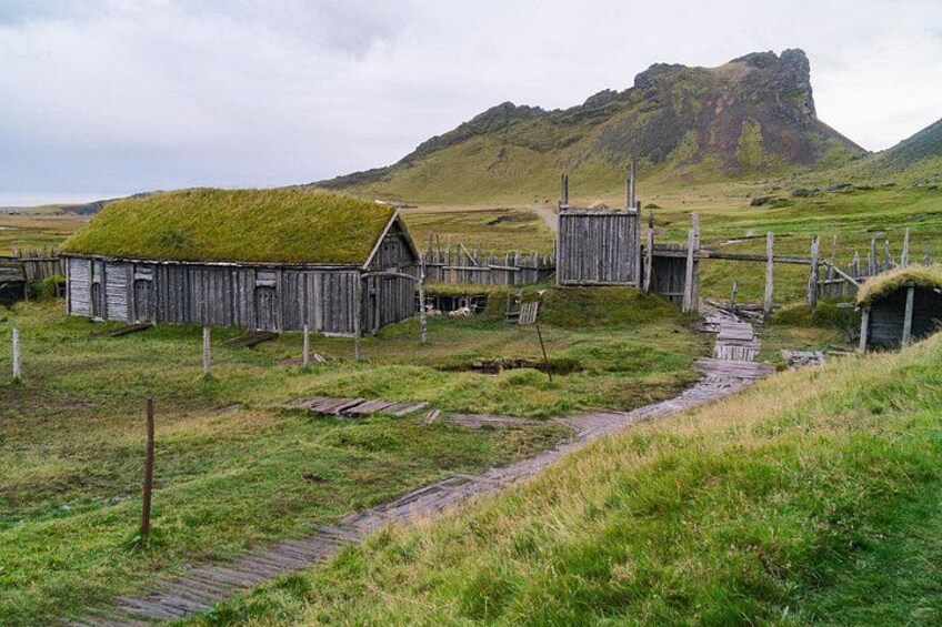 A rural landscape with a grassy hill, a wooden structure with a thatched roof, and a wooden bridge. 4