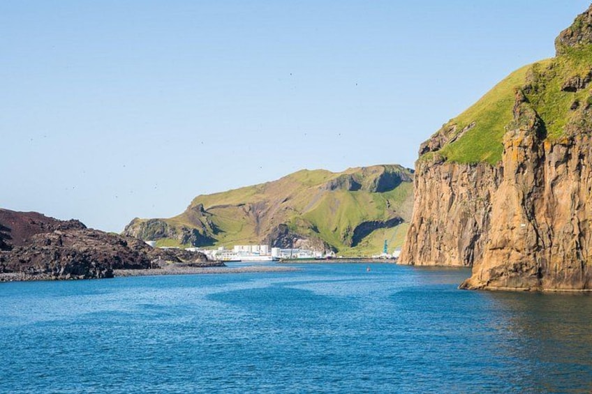 A coastal landscape with a clear blue sea, rocky cliffs, and a building in the distance. 3