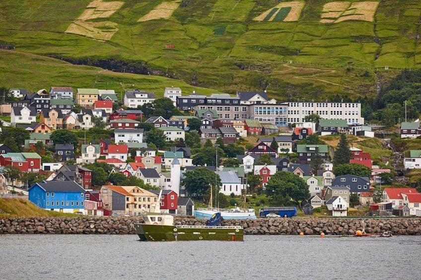 A coastal village with colorful houses, a large white building, and a green boat in the water. 2