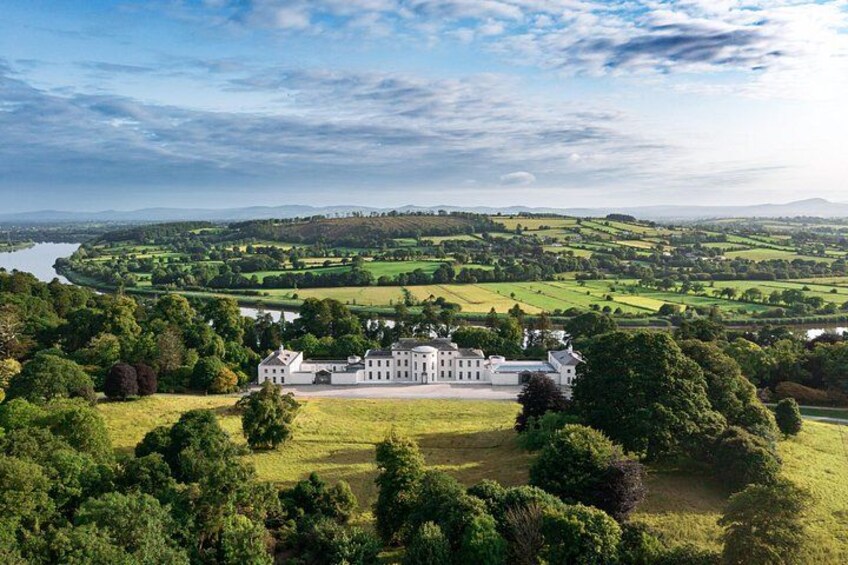 A large estate with a white building surrounded by lush greenery and a river in the background. 2