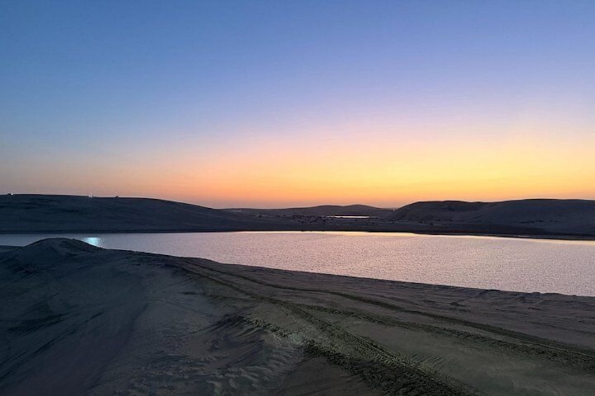 A sunset over a desert landscape with a body of water and distant hills. 3