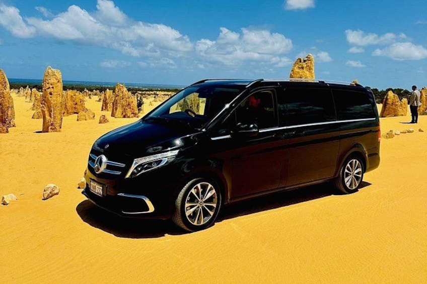 A black minivan parked on a sandy desert with rock formations in the background. 1