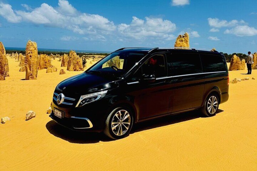 A black minivan parked on a sandy desert with rock formations in the background. 1