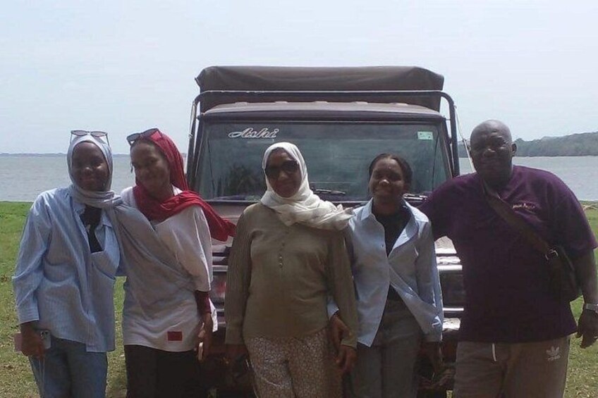 A group of people standing in front of a vehicle by a body of water. 5