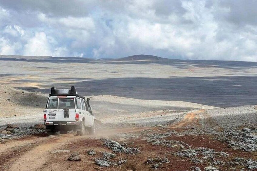 Un vehículo blanco circulando por un camino de tierra en un paisaje árido con montañas a la distancia. 4