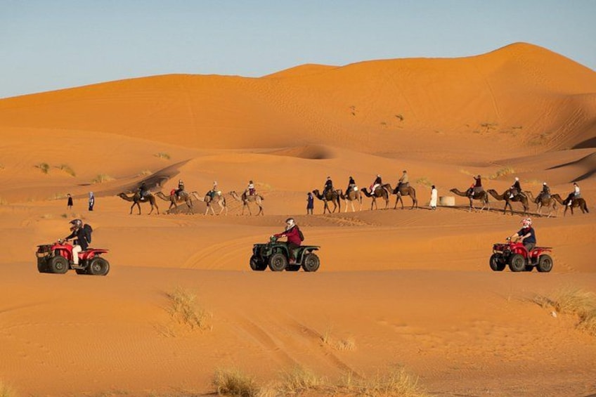 Paisaje desértico con dunas de arena, personas montando camellos y vehículos todo terreno. 1