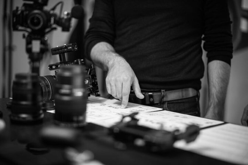 A person pointing at a table with a camera and lenses. 1