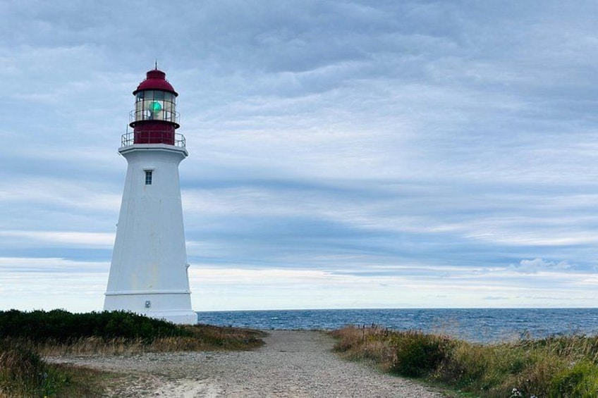 Un phare blanc avec un sommet rouge, un chemin de gravier menant à celui-ci, et une étendue d’eau en arrière-plan. 4