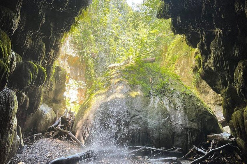 Une grotte avec une cascade, des rochers couverts de mousse et la lumière du soleil qui filtre à travers. 1