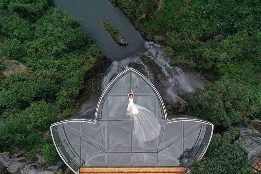 A person in a white dress standing on a glass structure with a waterfall in the background. 1
