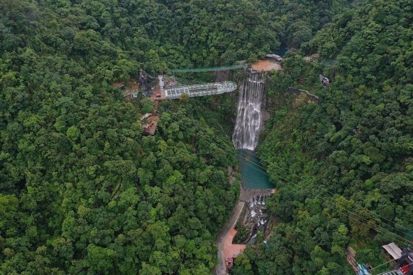 A waterfall cascading into a forested valley with a bridge and a small building. 2