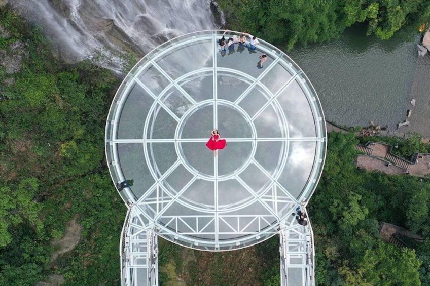 An aerial view of a glass-domed observation deck with people walking on it, surrounded by lush greenery and a river. 5