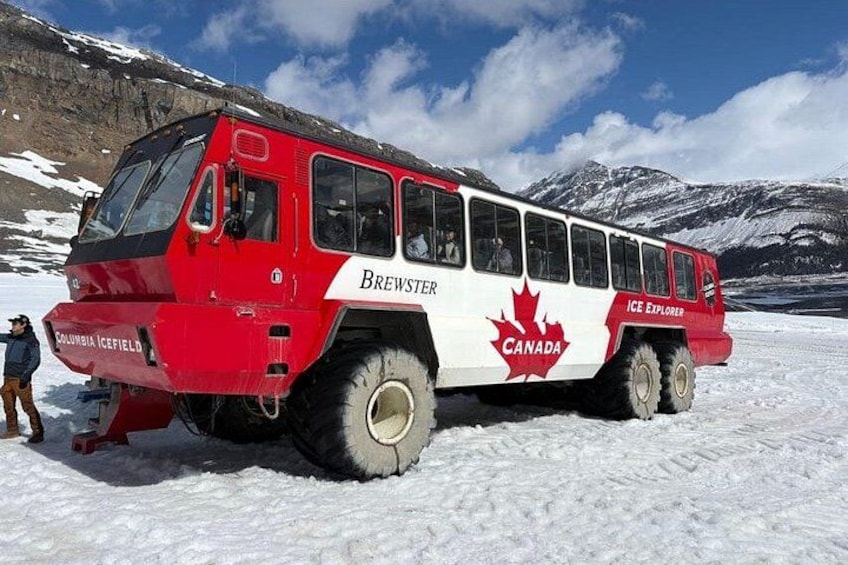 A red and white bus labeled 'Brewster' and 'Ice Explorer' parked on a snowy landscape with mountains in the background. 3