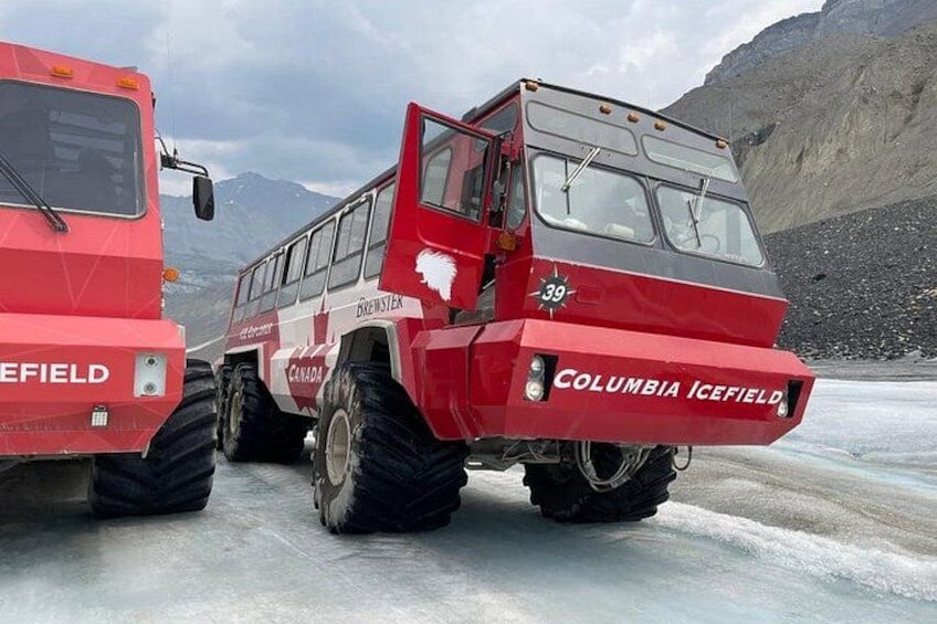 Two red ice field vehicles with 'COLUMBIA ICEFIELD' written on them, parked on a snowy surface with mountains in the background. 4