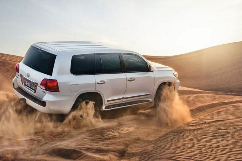 A white SUV driving through a desert with sand dunes. 1