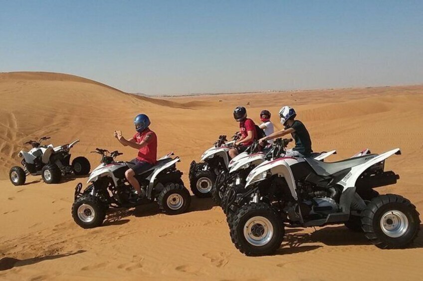 Four off-road vehicles on a sandy terrain with dunes in the background. 2