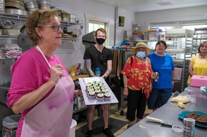 A group of people in a kitchen holding cupcakes and other baked goods. 5
