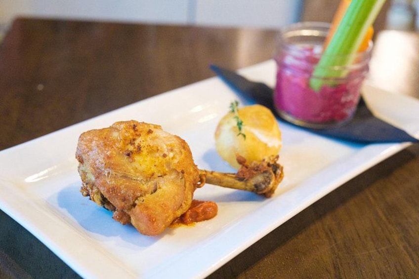 A plate with a roasted chicken leg and a small baked potato, accompanied by a drink with a celery stick. 2