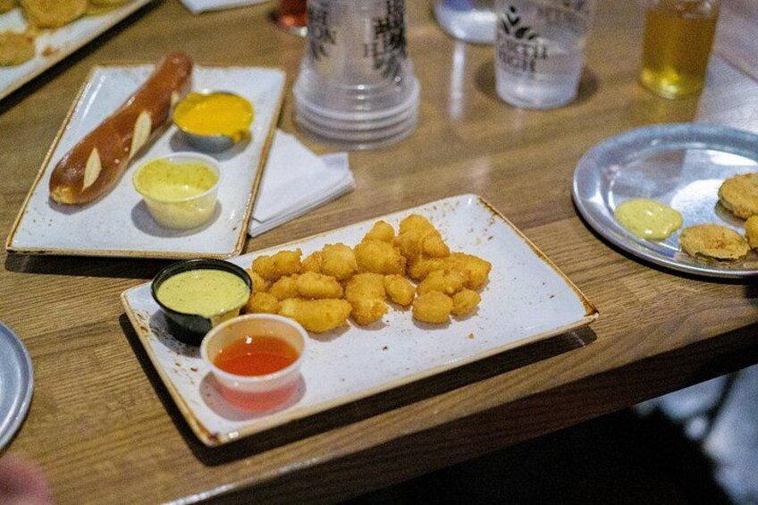 A wooden table with plates of food, including a hot dog, tater tots, and dipping sauces. 3