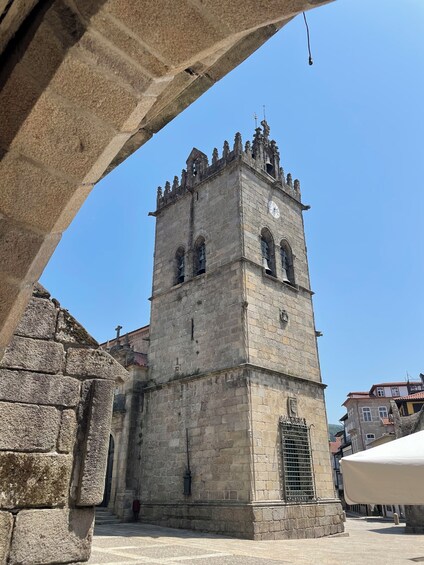 Una torre de piedra con un reloj y ventanas arqueadas, rodeada de muros y edificios de piedra. 1