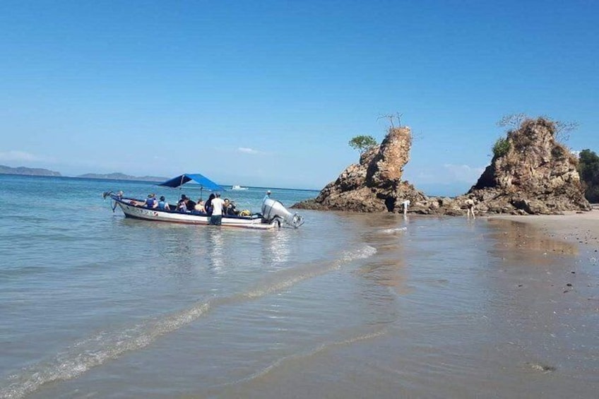 A boat on calm water, a rocky outcrop, and a clear sky. 1