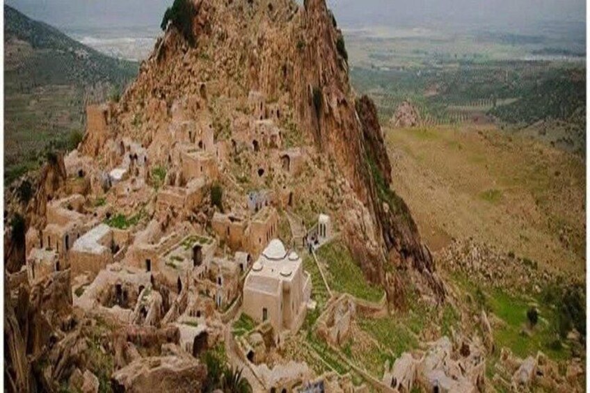 A mountainous village with traditional architecture, terraced fields, and a prominent rocky peak. 3