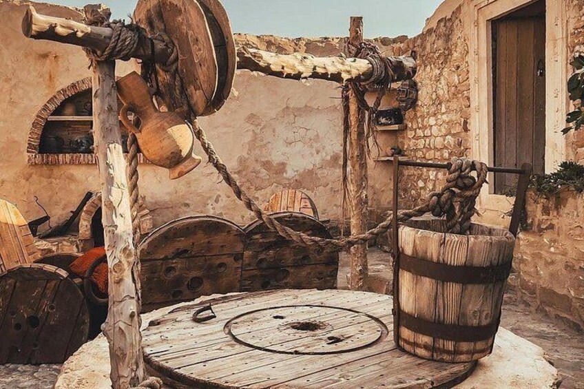 A traditional water pump with a wooden wheel and a barrel, set against a rustic stone wall. 2