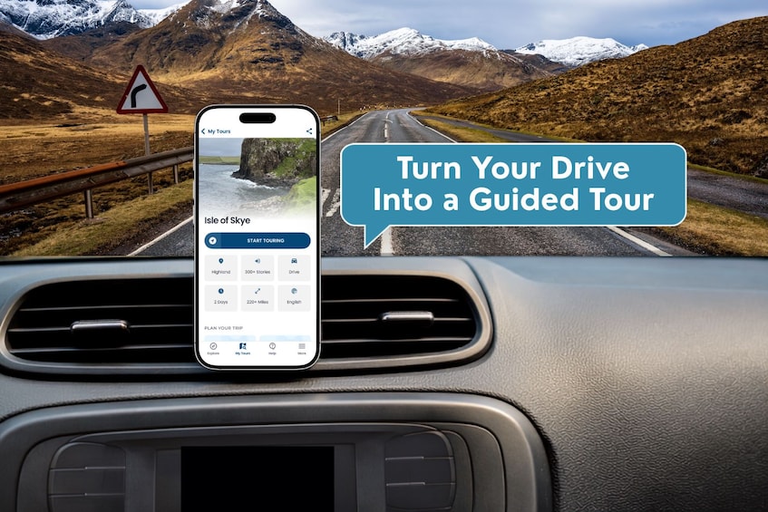 Een smartphone bevestigd aan een dashboard, waarop een app voor een begeleide tour staat, met een uitgestrekt berglandschap op de achtergrond. 4