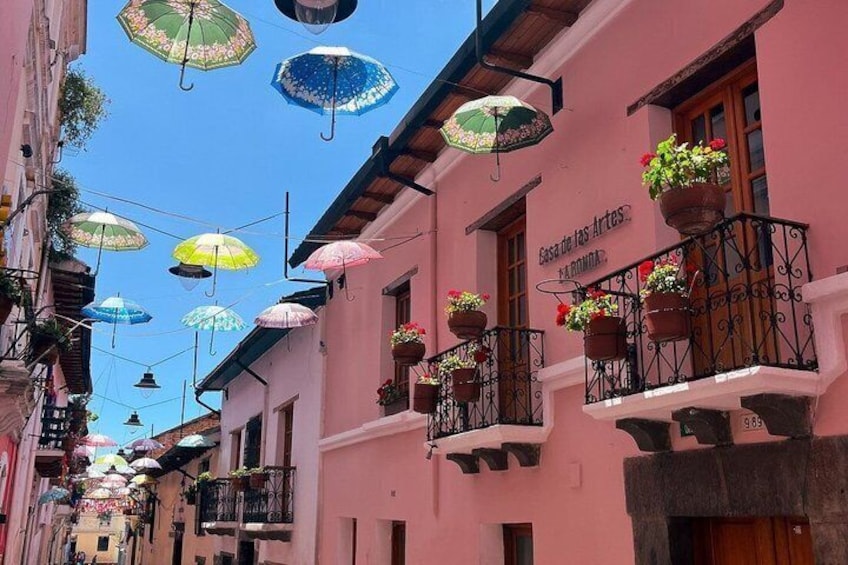 A narrow street with colorful umbrellas and flower baskets on balconies. 1