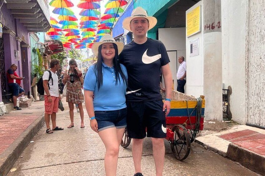 A street with colorful umbrellas, a man and woman in casual attire, and a cart. 2
