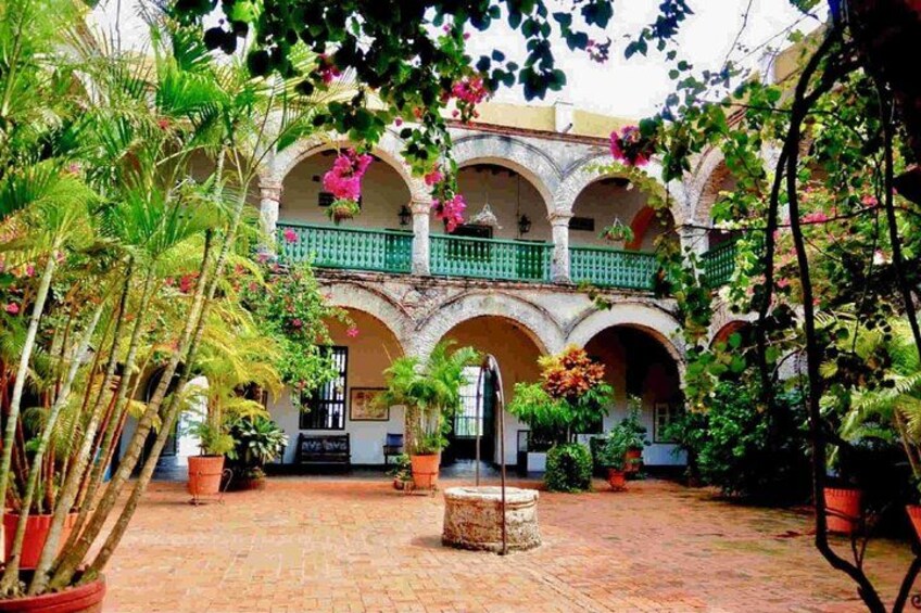 A courtyard with a brick floor, potted plants, and a building with arches and balconies. 3